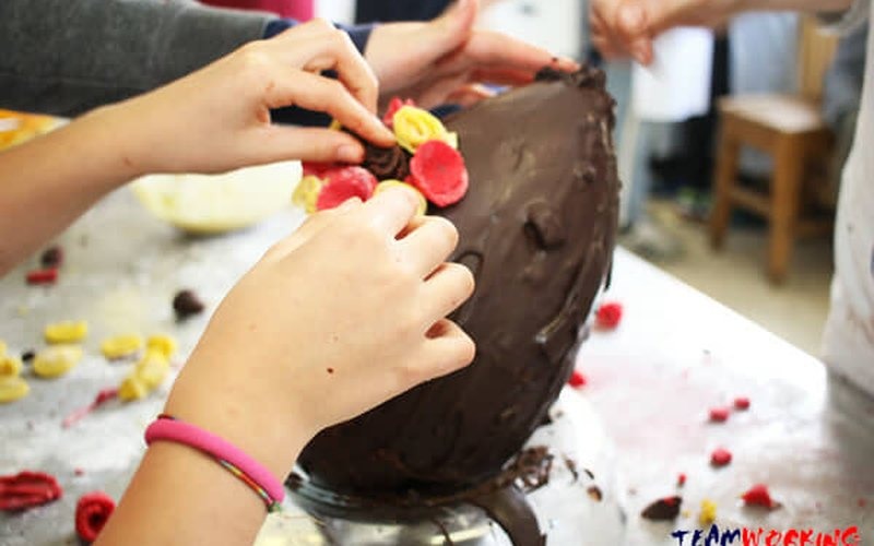 Mani che decorano un uovo di cioccolato con confetti colorati