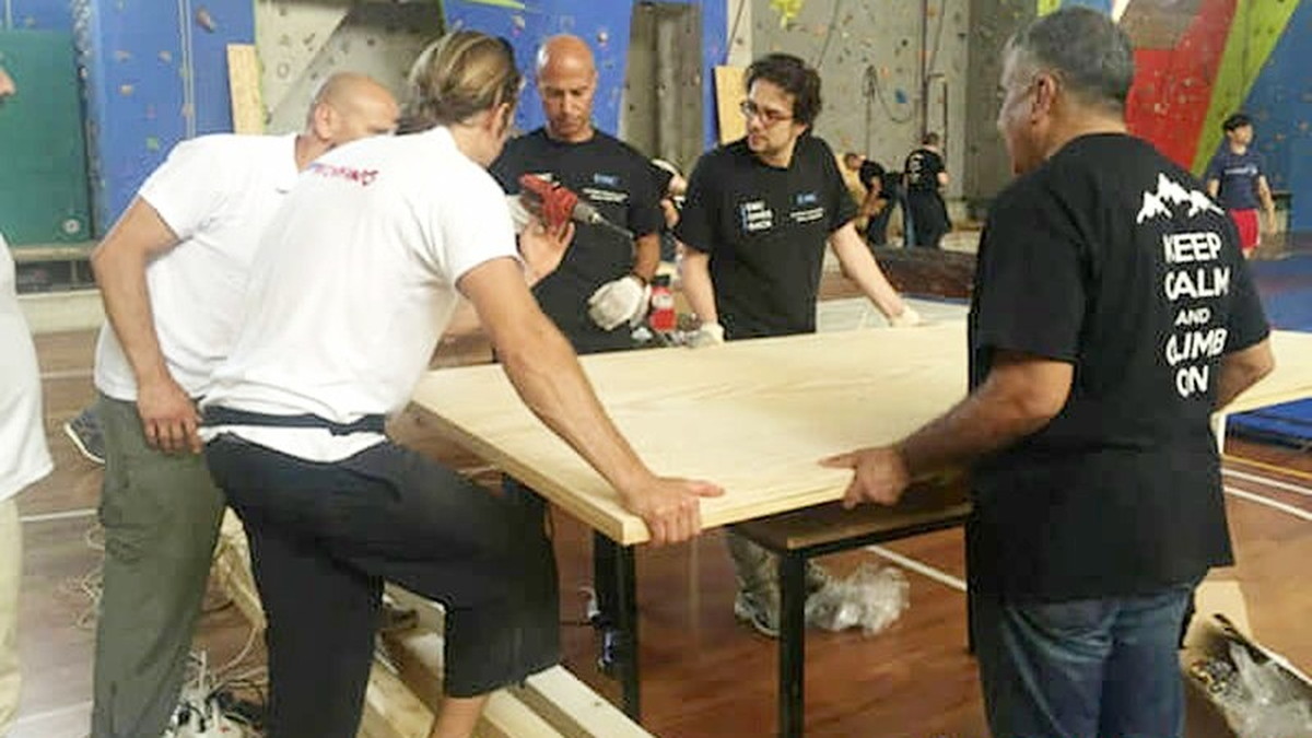 Quattro persone sollevano insieme un pannello di legno in una palestra di arrampicata