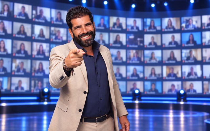 Un conduttore sul palco davanti al muro di schermi con tutta la squadra collegata