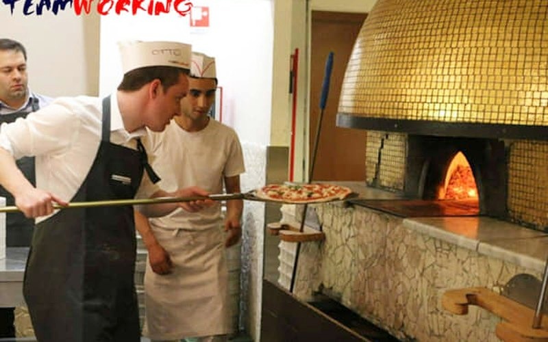 Un partecipante inforna una pizza nel forno a legna con la pala