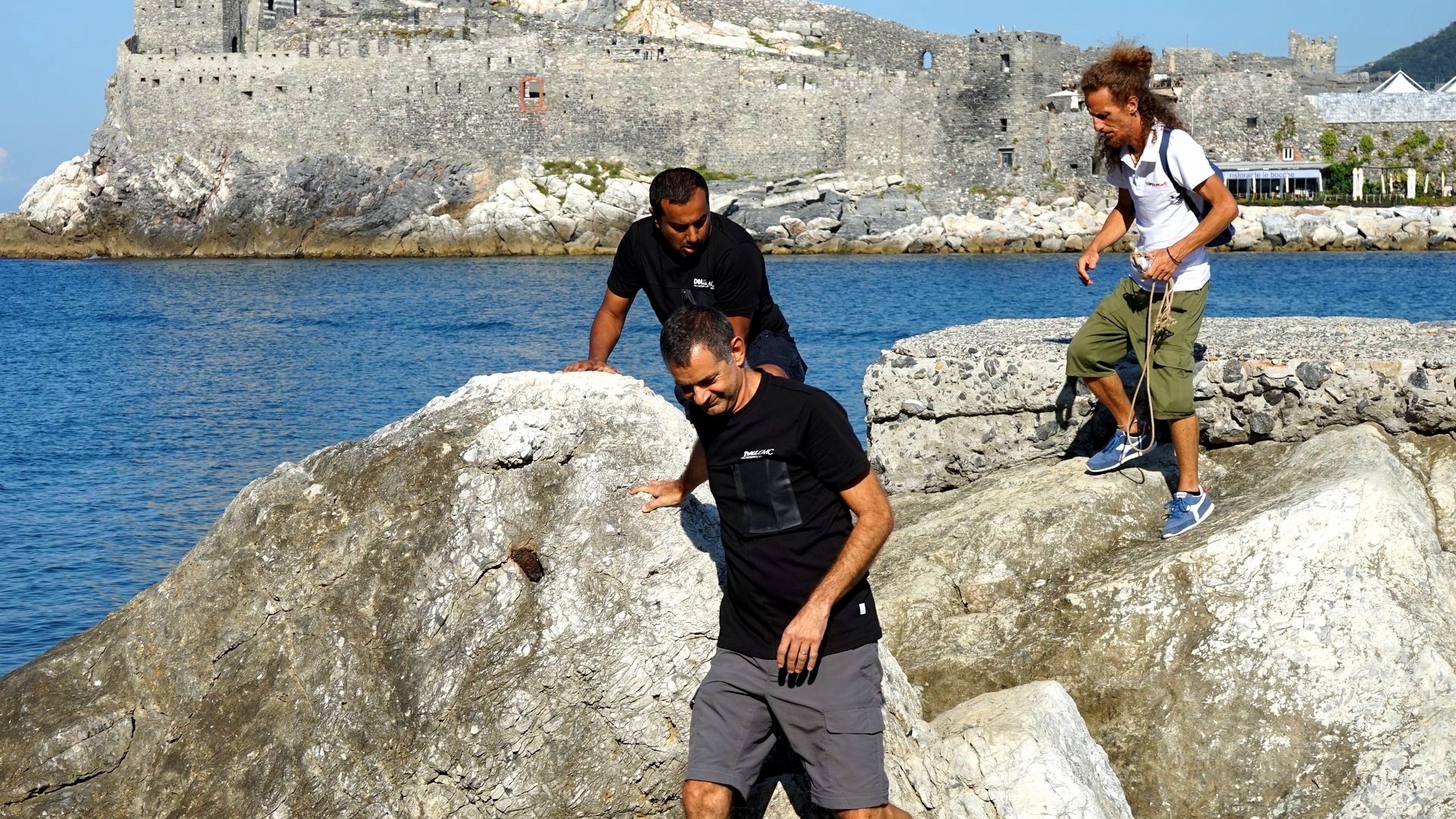 Gruppo di partecipanti attraversa un tratto di scogli lungo la riva