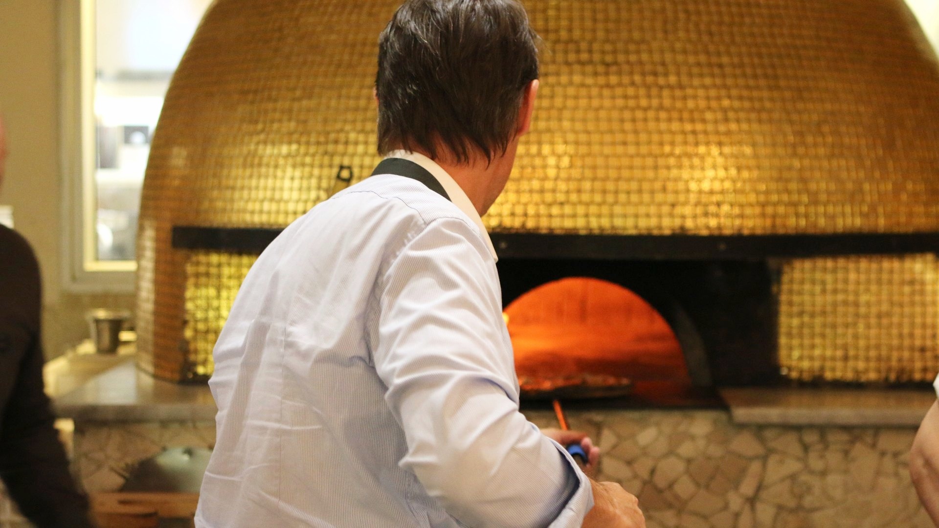 Il pizzaiolo al lavoro davanti alla bocca del forno a legna