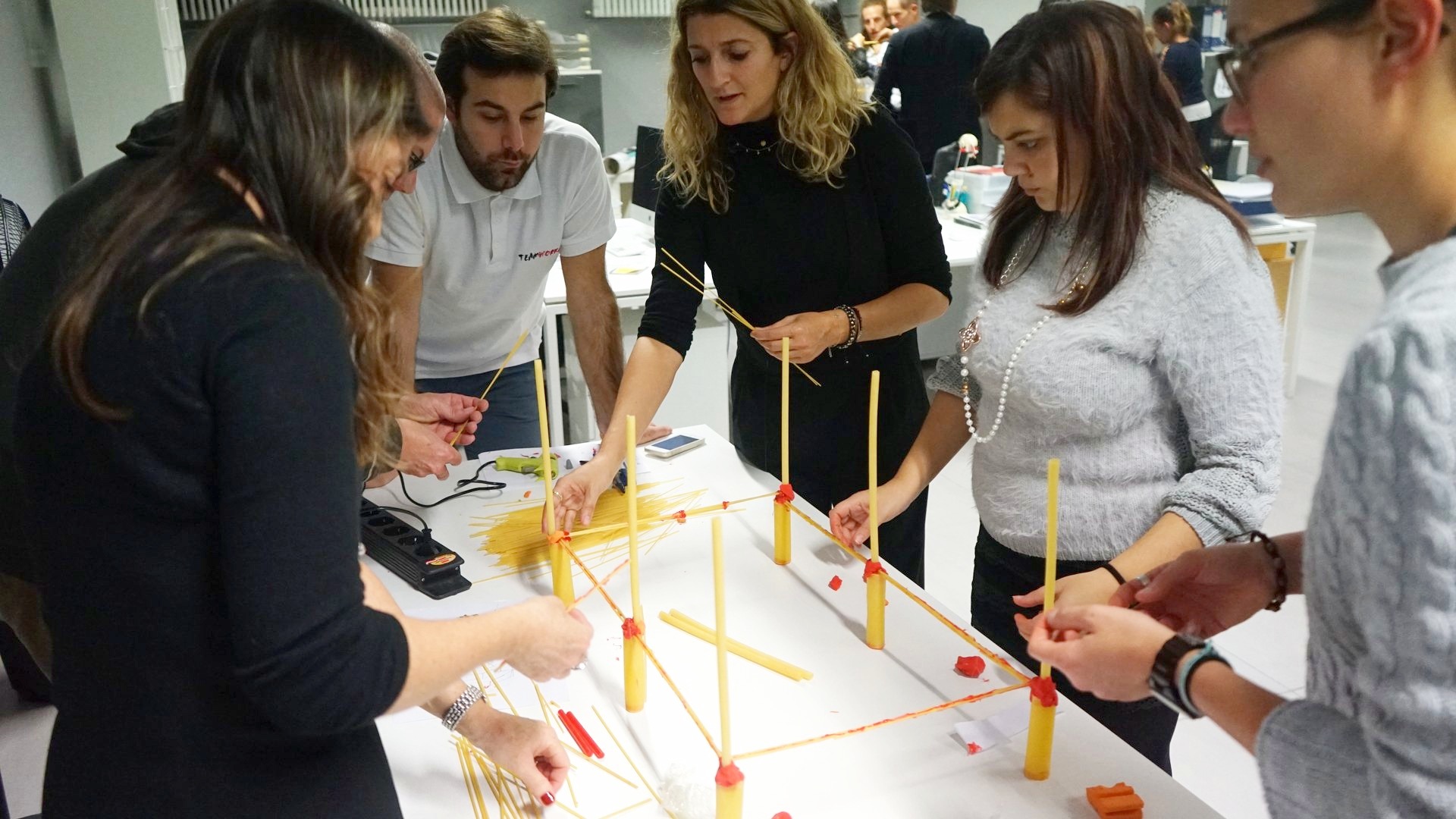 Cinque partecipanti costruiscono insieme una struttura di spaghetti sul tavolo