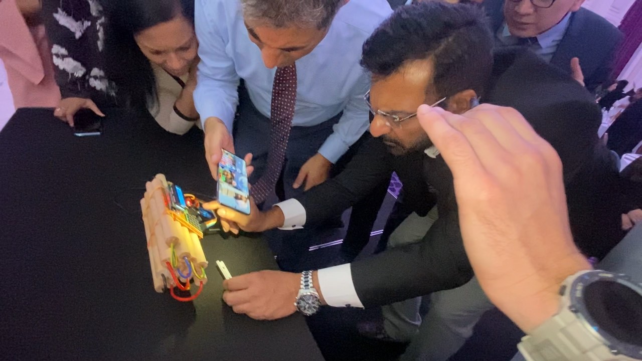 Partecipanti chini sul tavolo intorno al finto ordigno di una Escape Box, uno consulta il telefono mentre il tempo scorre