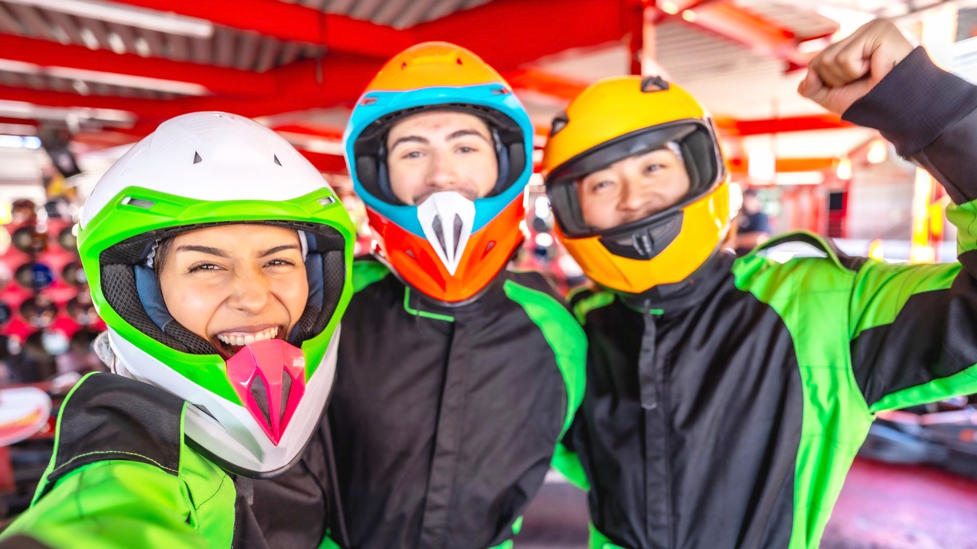 Tre partecipanti in tuta e casco ai box di un kartodromo