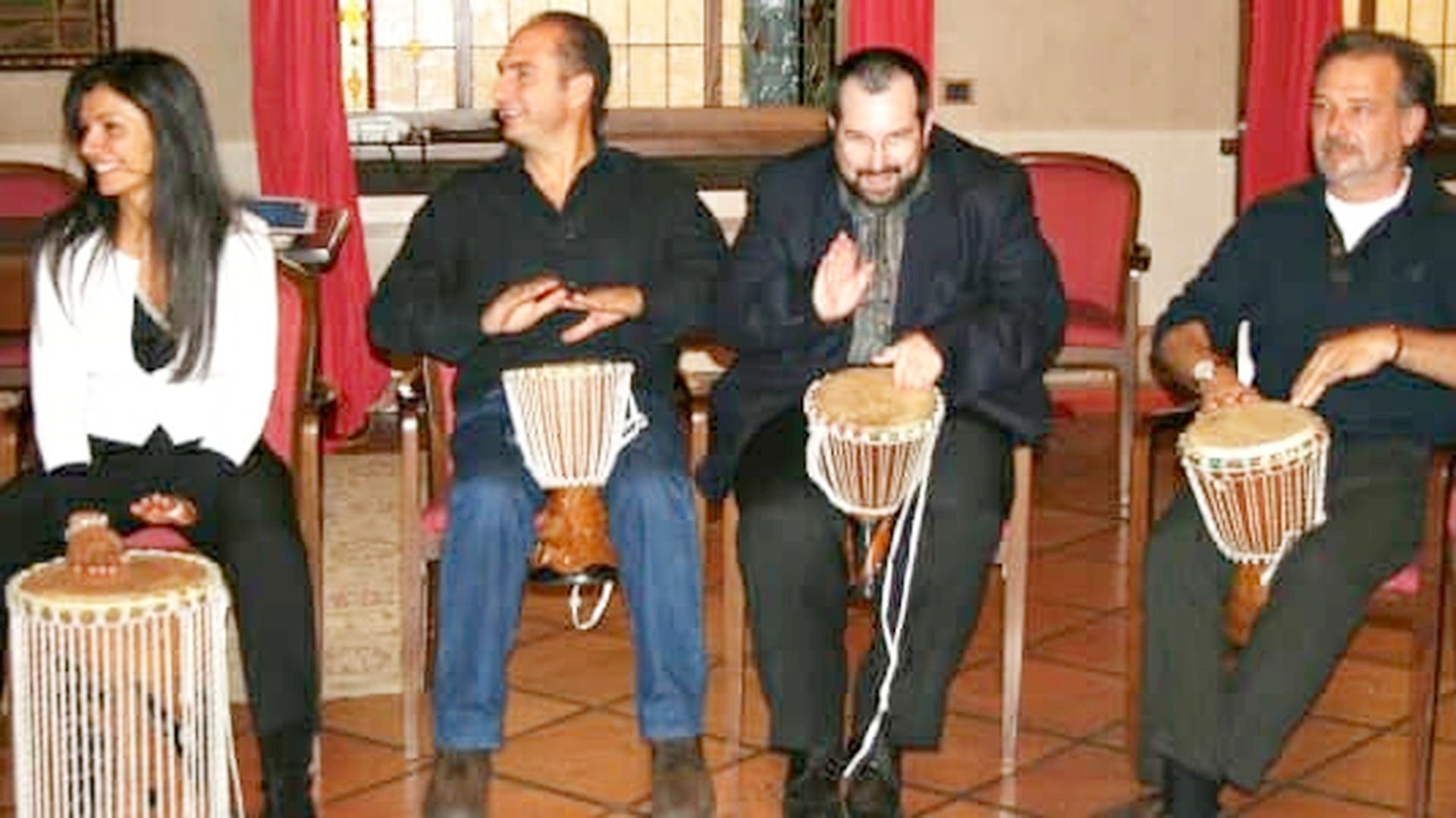 Partecipanti seduti in cerchio suonano i tamburi durante una sfida musicale