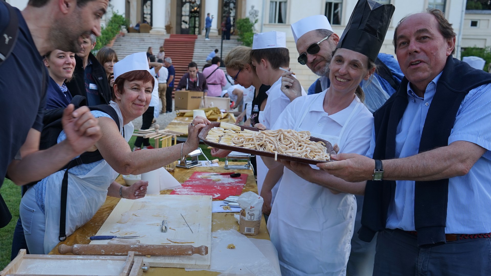Una squadra alza il vassoio di spaghetti alla chitarra appena fatti, davanti alla facciata di una villa veneta