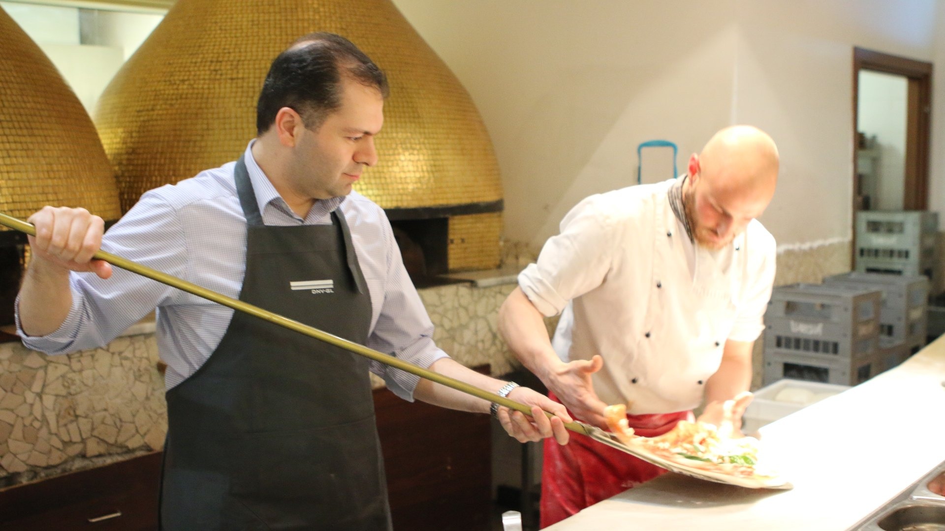 A pizzaiolo sliding a pizza into a wood-fired oven