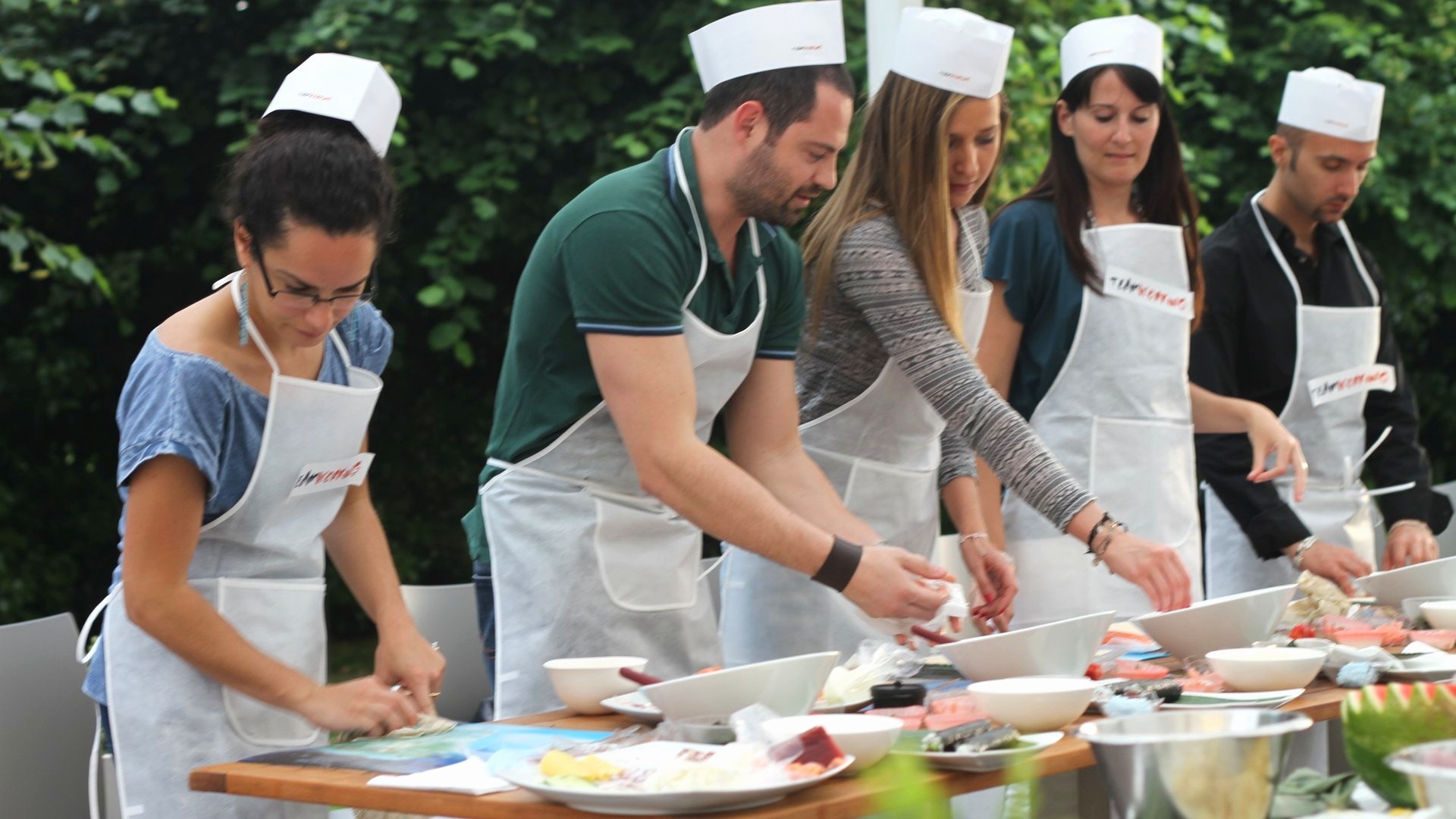Partecipanti in grembiule e cappello arrotolano il sushi al tavolo all'aperto