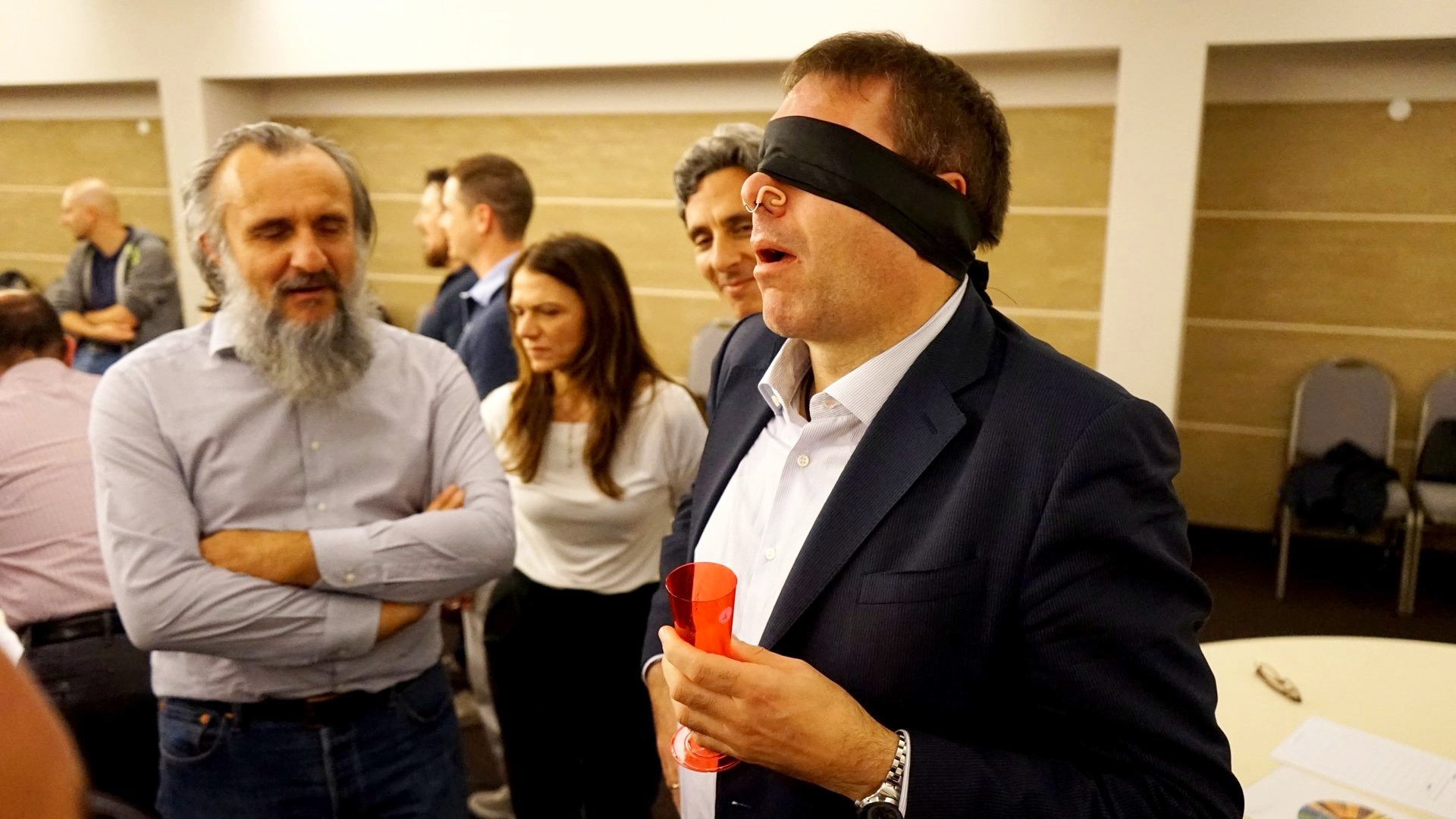 Un partecipante bendato assaggia da un calice mentre gli altri attendono il giudizio