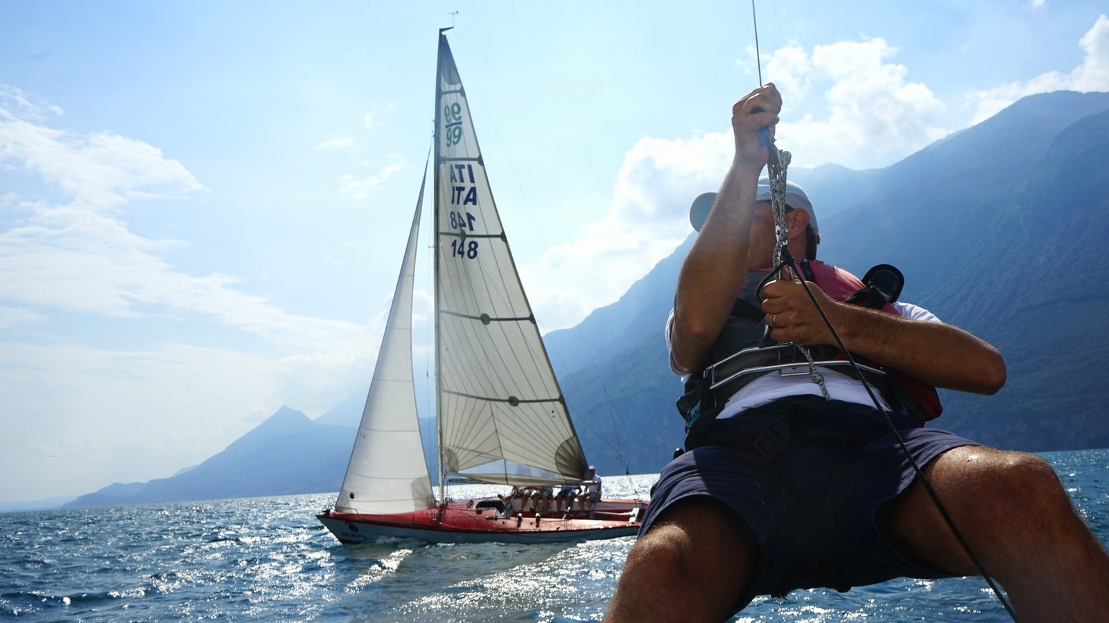 Un partecipante issa la randa mentre la barca a vela naviga sul lago fra le montagne